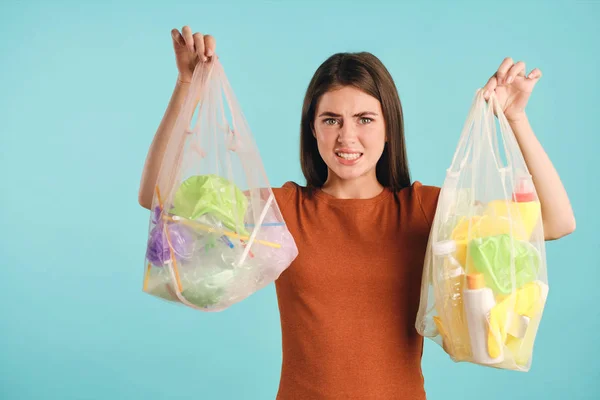 Emotioneel meisje squeamishly houden eco zakken met plastic afval en onaangenaam kijken in de camera over kleurrijke achtergrond — Stockfoto