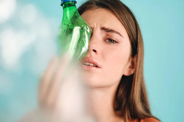 Портрет плачущей девушки, покрывающей лицо пустыми пластиковыми бутылками, печально смотрящей в камеру на красочном фоне — стоковое фото