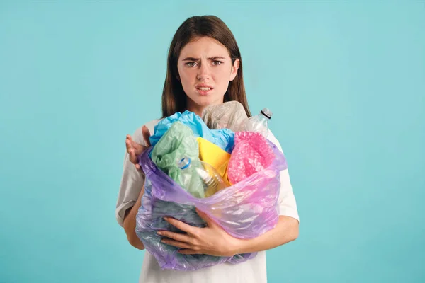 Zdenerwowana dziewczyna trzyma plastikowe odpady depresji patrząc w aparacie na kolorowe tło — Zdjęcie stockowe