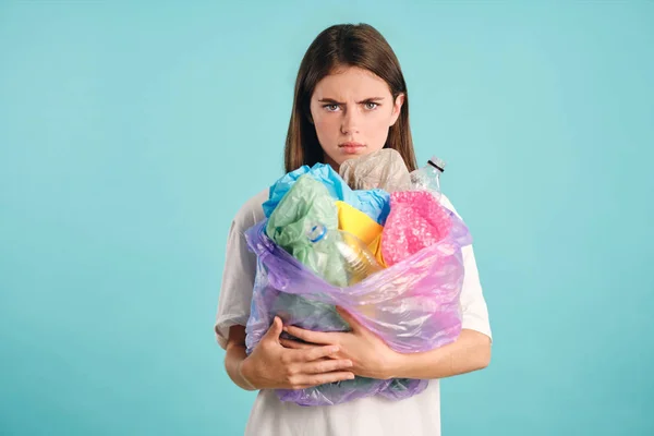 Menina irritada segurando resíduos de plástico, infelizmente, olhando na câmera sobre fundo colorido — Fotografia de Stock