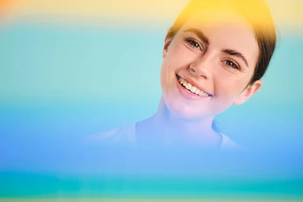 Begrepsbilder av en positiv smilende jente som gladelig ser i kamera gjennom regnbuen over fargerik bakgrunn – stockfoto