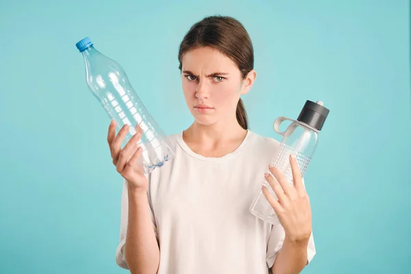 Gadis serius marah melihat di kamera memegang eko dan botol plastik di tangan atas latar belakang berwarna-warni — Stok Foto