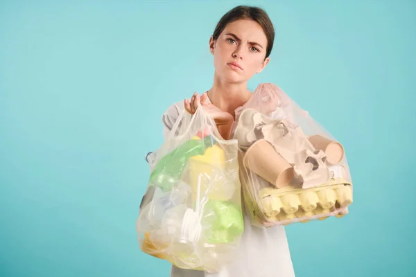 Menina perturbada segurando pacotes com classificação de plástico e caixas de lixo cansadamente olhando na câmera sobre fundo colorido — Fotografia de Stock