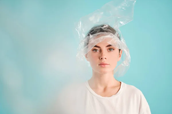 Серйозна дівчина з пластиковим пакетом на голові впевнено дивиться в камеру на барвистому фоні — стокове фото