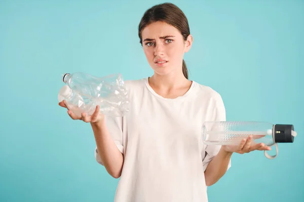 Upset girl sadly looking in camera holding eco and plastic bottles in hands over colorful background Stock Photo
