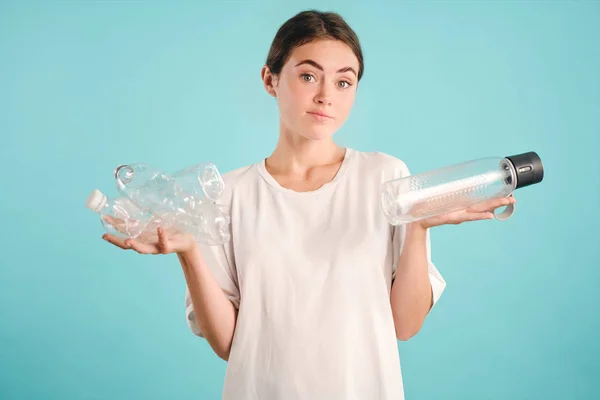 Fata atractivă care deține sticle de eco și plastic în mâini uitându-se atent în cameră pe fundal colorat Fotografie de stoc