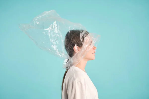 Vista lateral de chica con bolsa de plástico en la cabeza sobre fondo colorido Imagen De Stock
