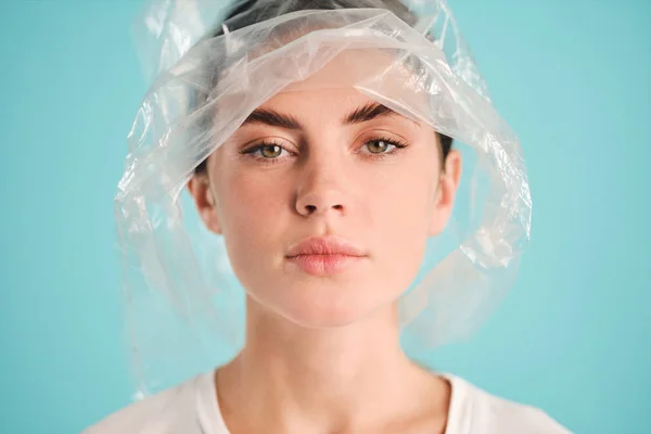 ผู้หญิงที่มั่นใจกับถุงพลาสติกบนหัว มองอย่างจริงจังในกล้องเหนือพื้นหลังที่มีสีสัน รูปภาพสต็อกที่ปลอดค่าลิขสิทธิ์