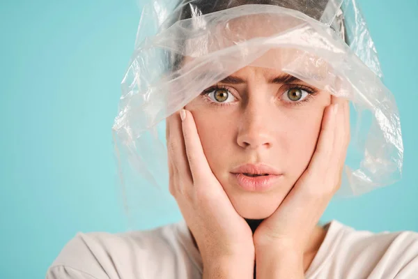 Close up upset girl with plastic bag on head scared looking in camera over colorful background Stock Picture