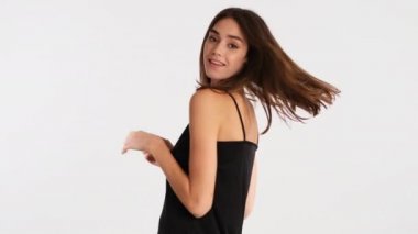 Çekici pozitif kahverengi saçlı kız beyaz arka planda neşeyle dans ediyor.