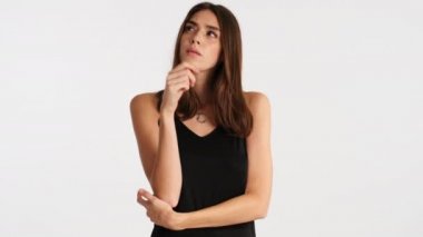 Çekici kahverengi saçlı kız düşünceli bir şekilde etrafına bakıyor ve mutlu bir şekilde beyaz arka plan üzerinde fikir yürütüyor.