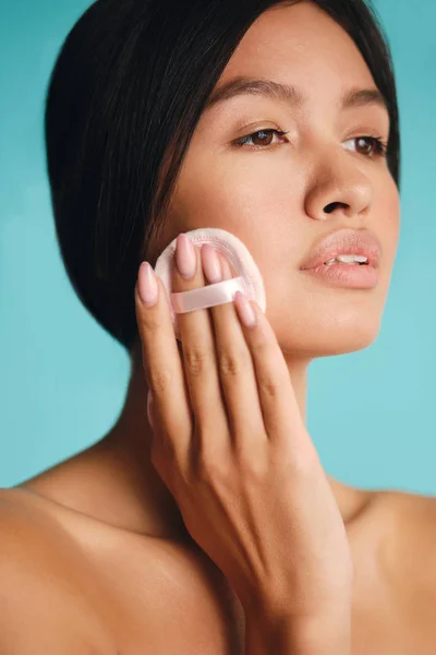 Retrato de bela menina morena asiática confiantemente usando sopro de pó sobre fundo colorido — Fotografia de Stock