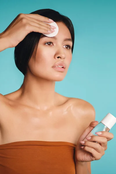 Atrakcyjne Azji brunetka dziewczyna uważnie patrząc z dala czyszczenia twarzy z gąbką na kolorowe tło — Zdjęcie stockowe