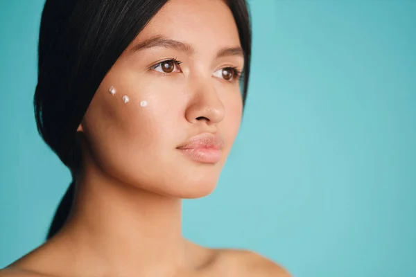 Close-up charmant aziatisch brunette meisje met punten van crème op wang poseren over kleurrijke achtergrond — Stockfoto