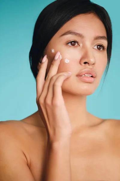 Bastante asiática morena chica con puntos de crema en mejilla soñando posando sobre colorido fondo —  Fotos de Stock