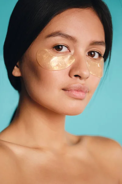 Közelkép vonzó ázsiai lány foltok alatt szemek magabiztosan nézi a kamera felett színes háttér — Stock Fotó