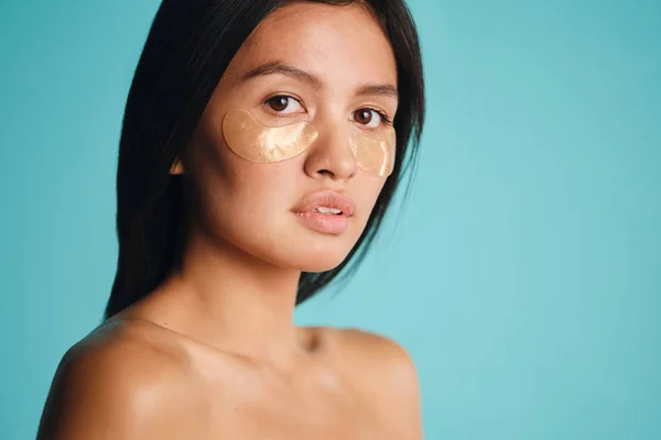 Attractive Asian girl with patches under eyes thoughtfully looking in camera over colorful background — Stock Photo, Image