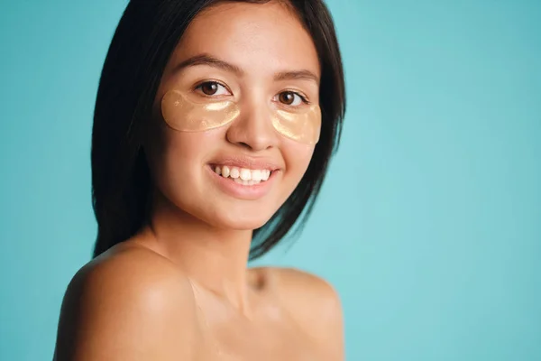 Bastante alegre asiático chica con parches bajo los ojos felizmente mirando en cámara sobre colorido fondo —  Fotos de Stock