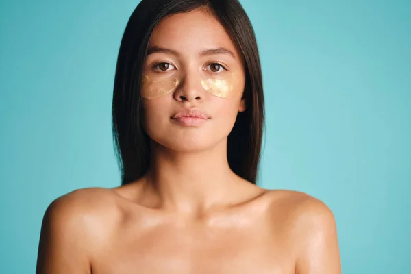 Gyönyörű ázsiai barna lány foltok alatt szemek magabiztosan nézi a kamera felett színes háttér — Stock Fotó
