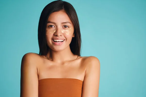 Pretty smiling Asian girl with patches under eyes joyfully looking in camera over colorful background — Stock Photo, Image