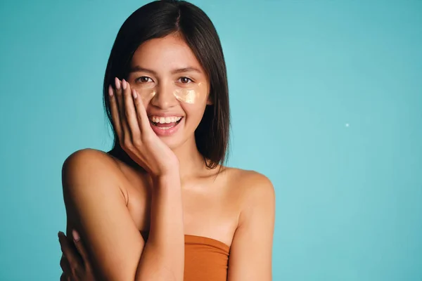 Beautiful smiling Asian girl with patches under eyes joyfully posing over colorful background — Stock Photo, Image