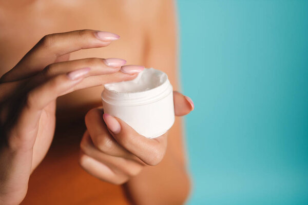 Закройте руки женщине держа банку крема красоты на синем фоне
