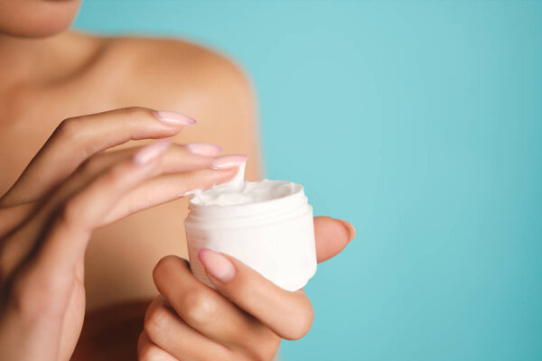 Close up young woman holding jar of beauty cream over colorful background