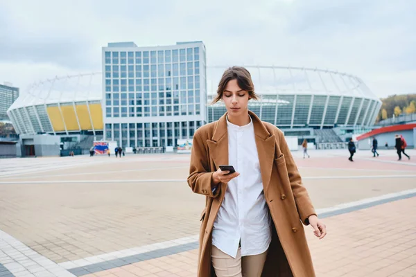 Молодая красивая стильная женщина в пальто с сотовым телефоном ходить по улице города — стоковое фото