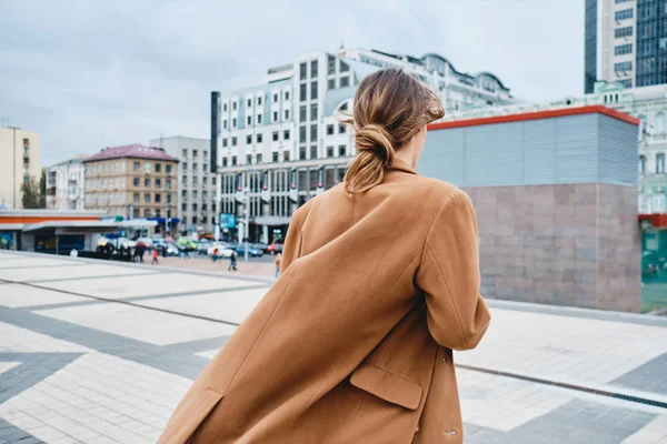 Kembali melihat wanita muda bergaya mantel percaya diri berjalan melalui jalan kota — Stok Foto