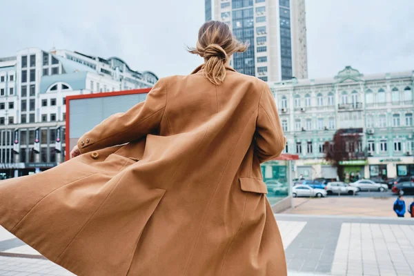 Вид на молодую привлекательную стильную женщину в пальто, мечтательно идущую по городской улице — стоковое фото