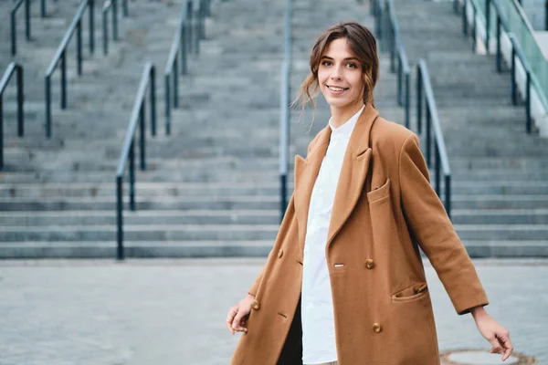 Młoda atrakcyjna stylowa kobieta w płaszczu szczęśliwie patrząc w aparacie na zewnątrz — Zdjęcie stockowe