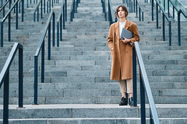 Młoda atrakcyjna bizneswoman w płaszczu z laptopem starannie patrząc na zewnątrz — Zdjęcie stockowe