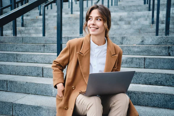 Jovem mulher de negócios atraente no casaco com laptop alegremente olhando para longe nas escadas na rua — Fotografia de Stock