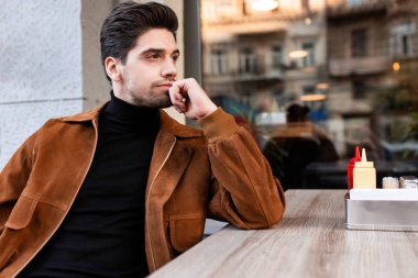 Genç, çekici, sıradan bir adam, düşünceli bir şekilde caddedeki kafeye bakıyor.