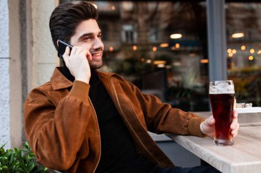 Genç, yakışıklı, sıradan bir adam cep telefonuyla konuşuyor, elinde birayla sokakta oturuyor.