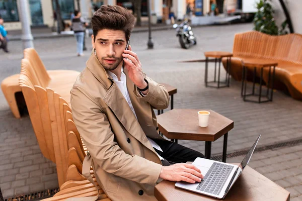 캐치 코트를 입고 카페에서 노트북을 가지고 일하면서 생각깊은 이야기를 하는 젊은 우연 한 사업가 — 스톡 사진