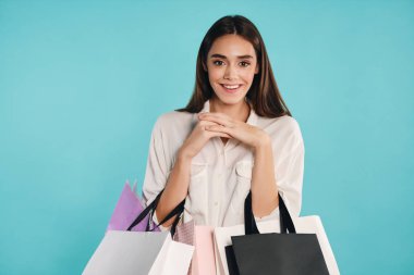 Alışveriş torbalarıyla oldukça olumlu bir kız. Renkli arka planda kameraya bakıyor.