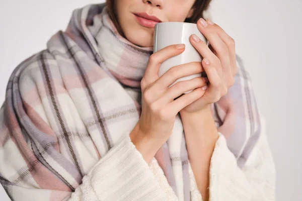 Close up ragazza attraente con accogliente sciarpa in possesso di tazza con bevanda calda vicino al viso su sfondo bianco — Foto Stock