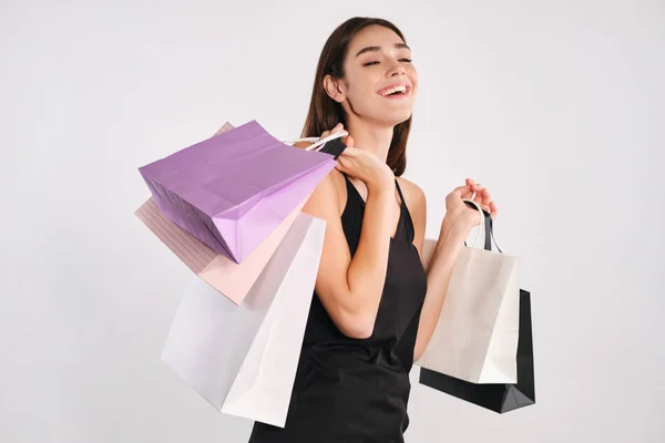 Ziemlich fröhliches Mädchen mit Einkaufstaschen glücklich in die Kamera vor weißem Hintergrund blickend — Stockfoto