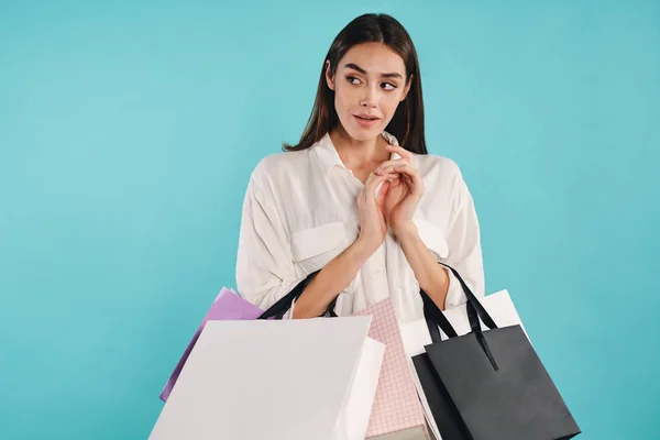 Atractiva chica casual con bolsas de compras astutamente mirando hacia otro lado sobre fondo colorido — Foto de Stock