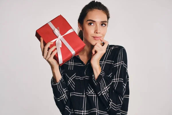 Hermosa chica casual alegre sosteniendo caja de regalo en la mano soñando sobre fondo gris —  Fotos de Stock