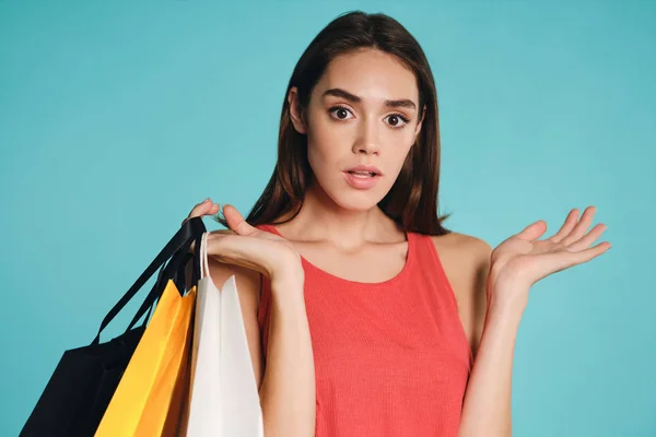 Meglepett alkalmi lány bevásárló táskák figyelmesen nézett a kamera felett színes háttér — Stock Fotó