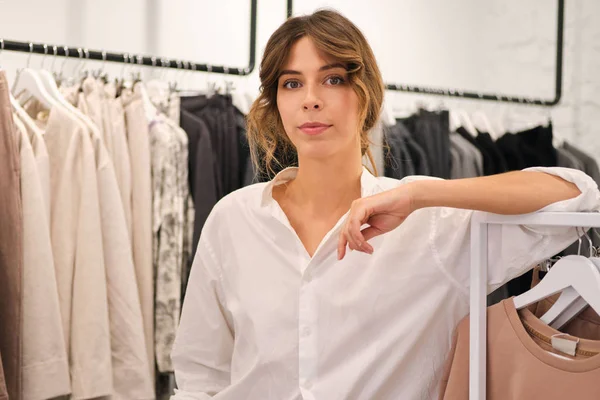 Młoda stylowa kobieta w koszuli uważnie patrząc w aparacie pracującym w nowoczesnym sklepie odzieżowym — Zdjęcie stockowe