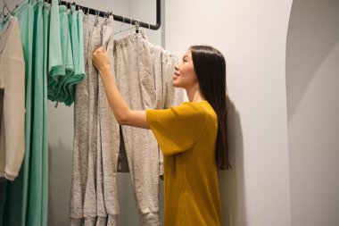 Güzel Asyalı kız modern moda mağazasında kıyafet seçerken mutlu oluyor.