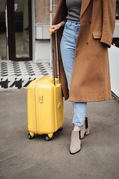 Κοντινό πλάνο casual κορίτσι σε παλτό στέκεται με κίτρινη βαλίτσα εξωτερική — Φωτογραφία Αρχείου