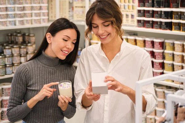 Jonge positieve consultant blij helpen om aroma kaars te kiezen voor mooie Aziatische meisje in moderne winkel — Stockfoto