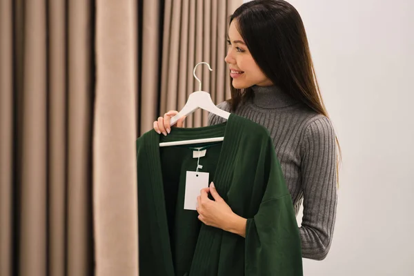 Vista laterale della bella ragazza asiatica sorridente che prova gioiosamente il cardigan nel moderno negozio di moda — Foto Stock
