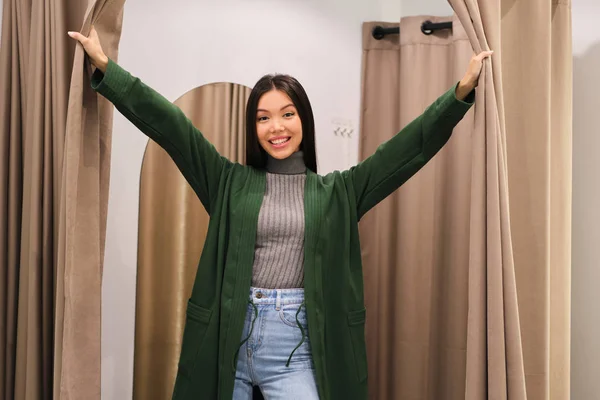 Pretty smiling Asian girl joyfully looking in camera from dressing room in modern fashion store — Stock Photo, Image