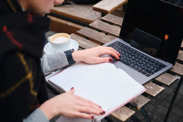 Close up estudante menina com café estudando no laptop com bloco de notas no café na rua — Fotografia de Stock