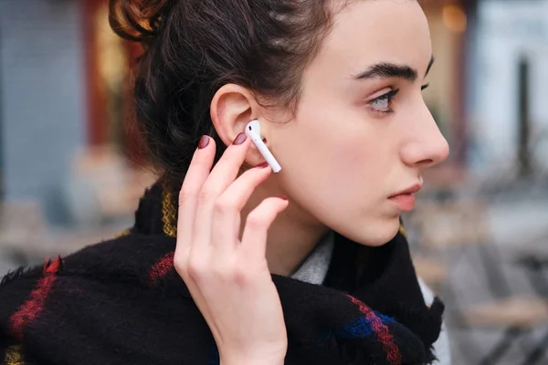 Pandangan samping gadis berambut cokelat yang cantik dengan earphone nirkabel sungguh-sungguh melihat ke luar — Stok Foto